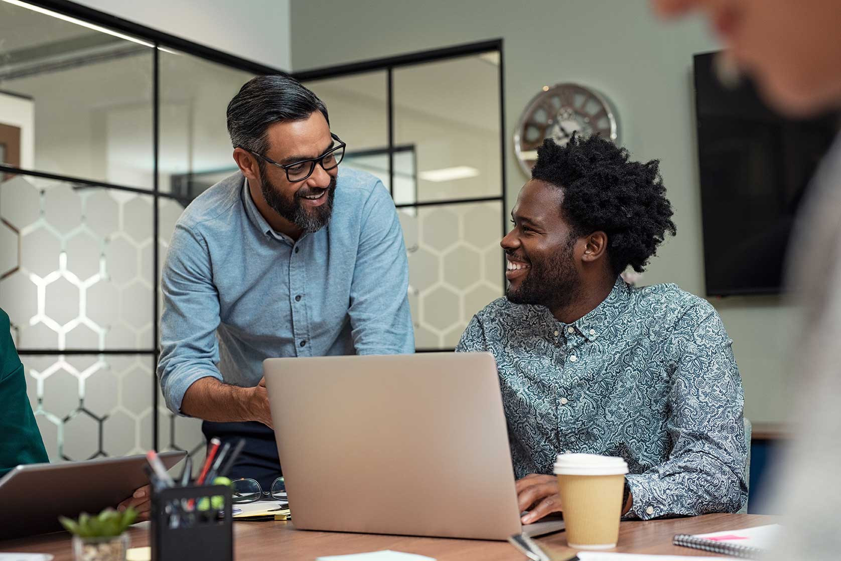 Two male colleagues smiling and discussing project while looking at laptop