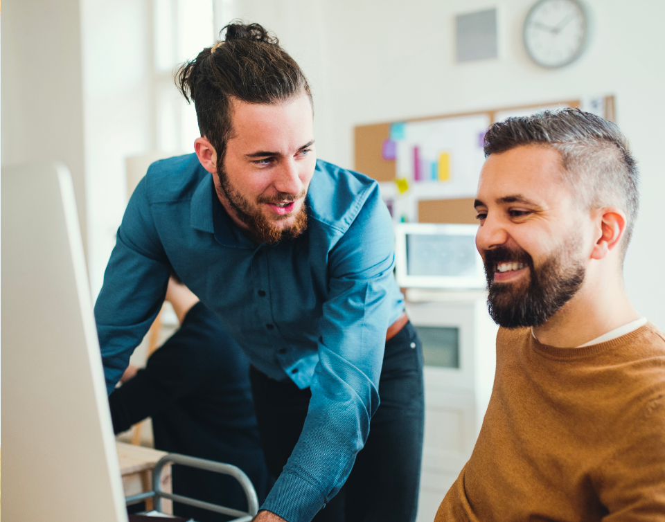 Two male teammates smiling and working at a desktop computer screen