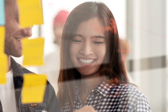 Woman smiling and reviewing post-it notes on window