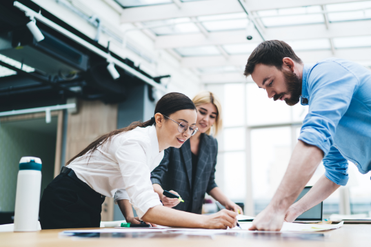 Three colleagues standing over a table, marking up mockups