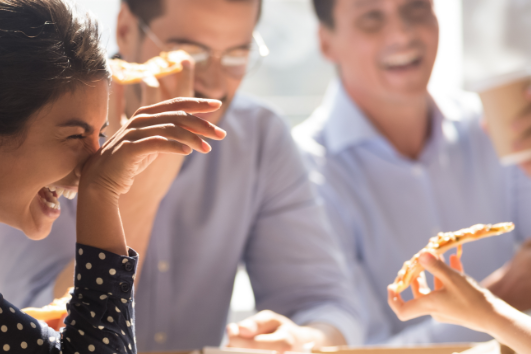 Team members enjoying pizza lunch together, laughing