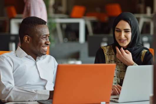 Male and female coworkers sitting together at their laptops smiling